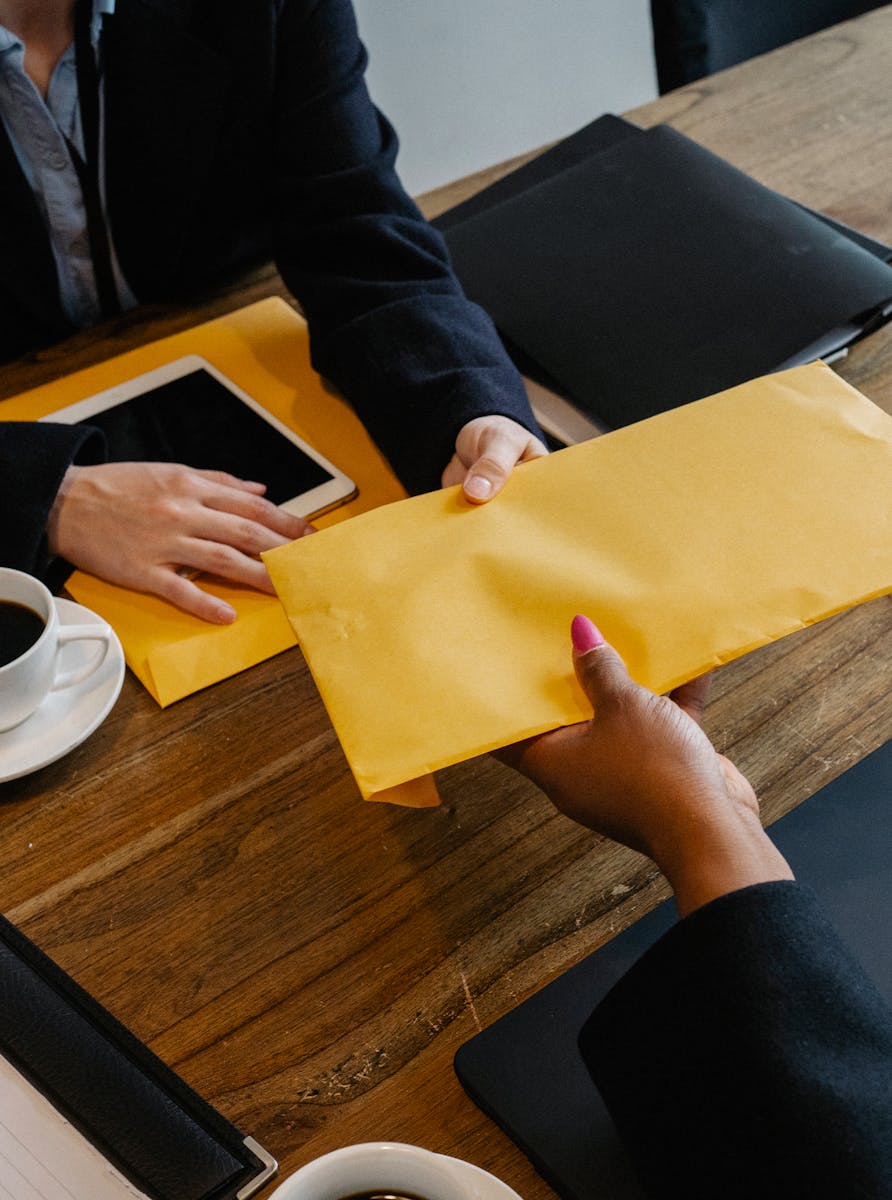Two business professionals exchange documents at a meeting table.